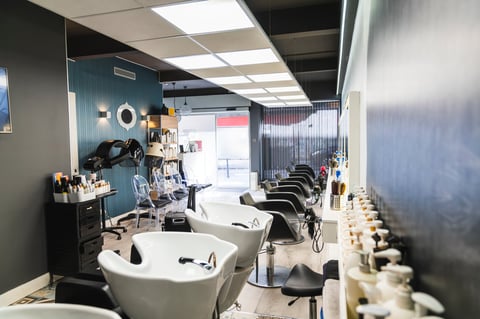 Empty, modern hairdressing salon displaying multiple styling chairs, shampoo washing sinks, and professional hair care products
