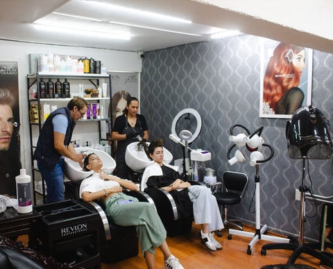 Professional makeup and styling studio with two artists working on clients seated in front of ring lights and mirrors